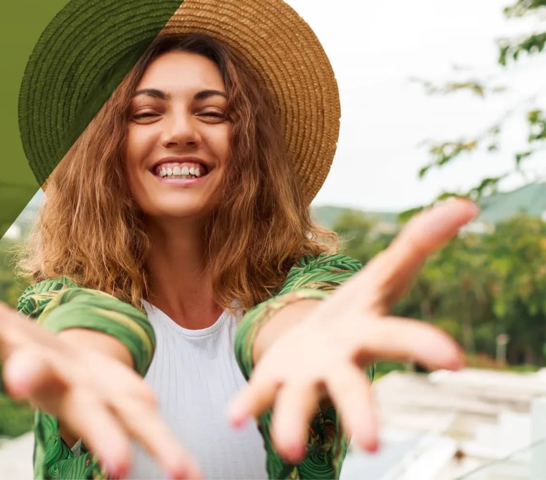 Una mujer sonriente con sombrero extiende los brazos hacia la cámara, al aire libre