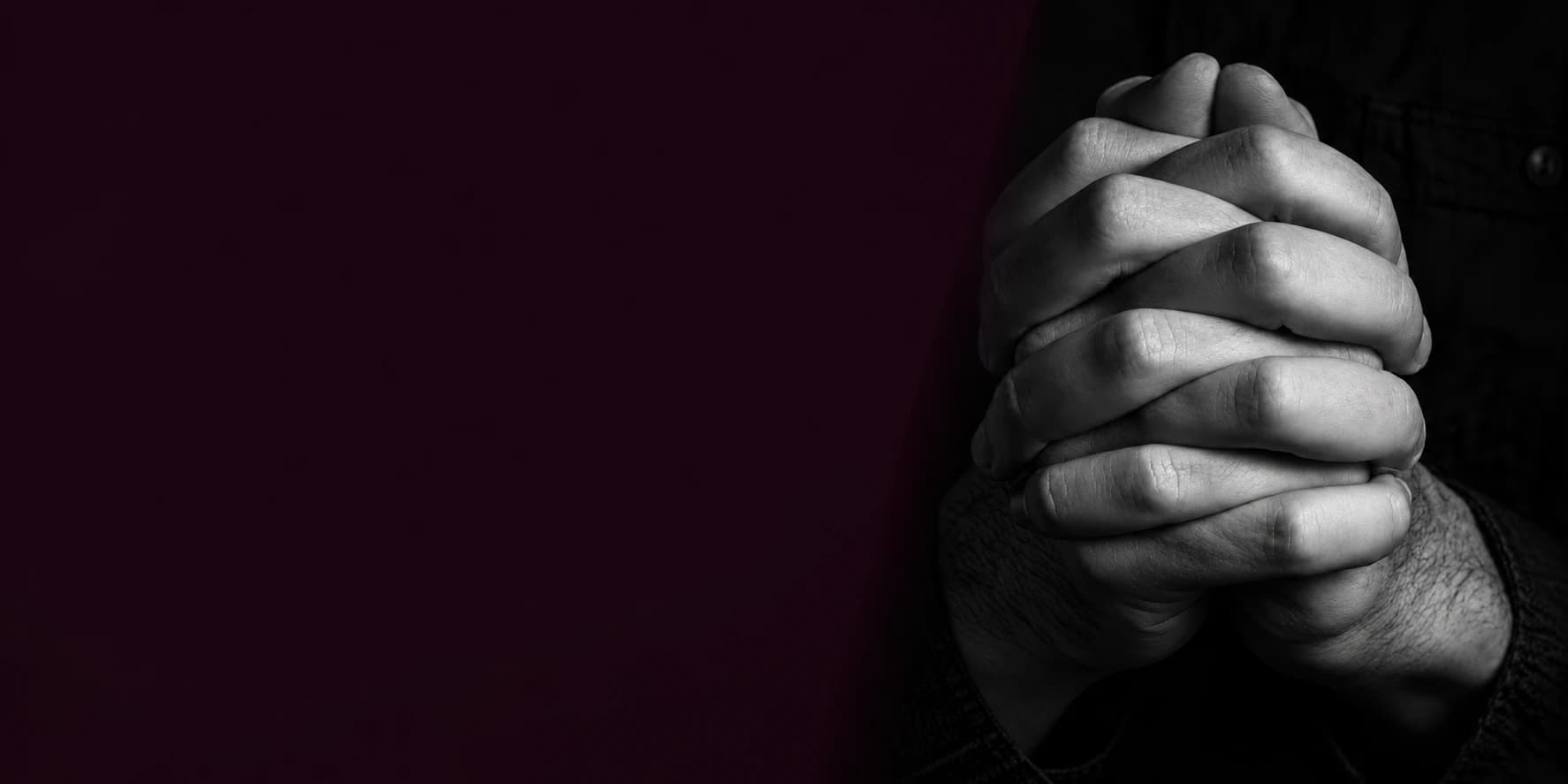 Un par de manos entrelazadas en oración, en blanco y negro, sobre el color del encabezado